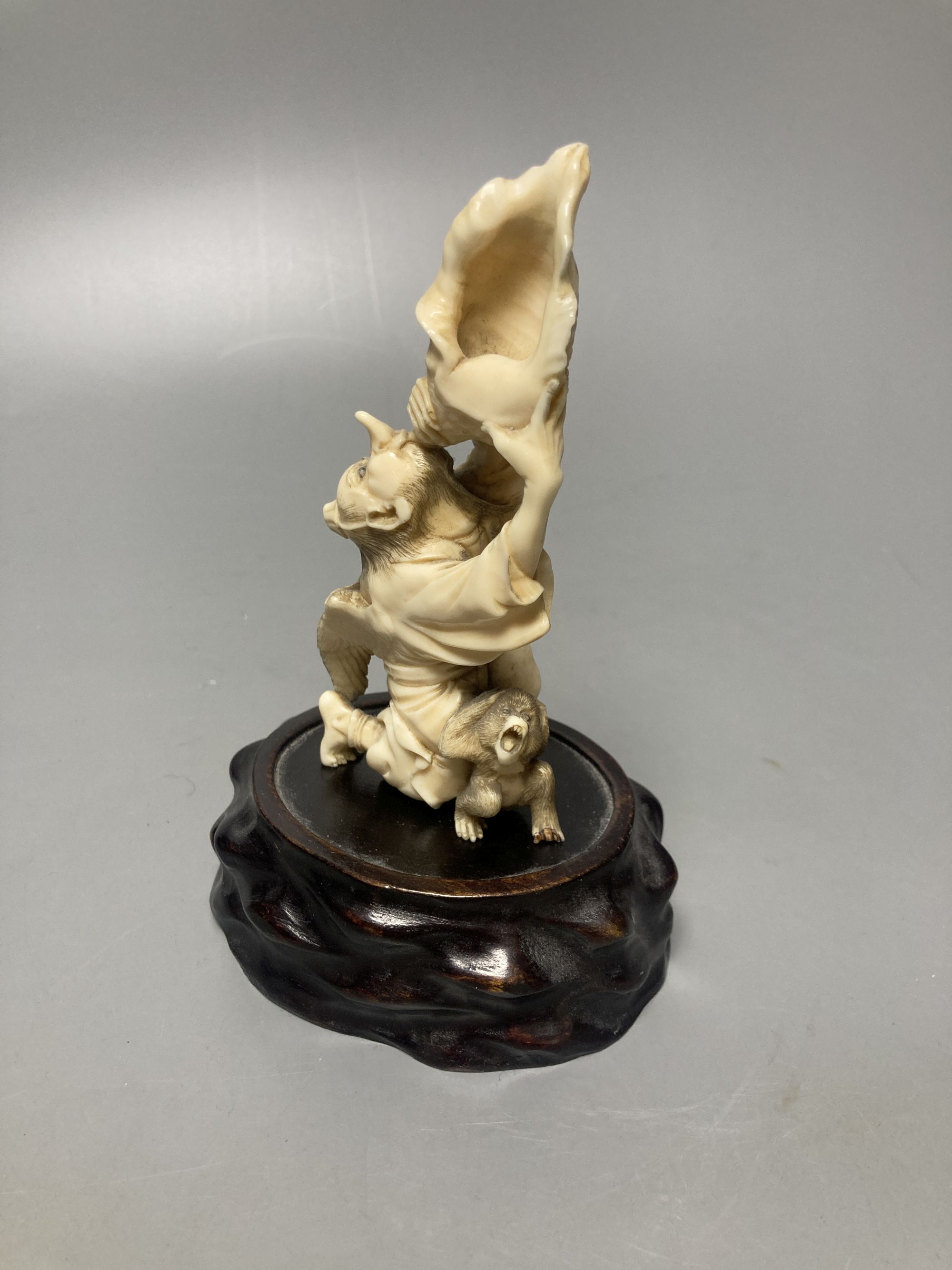 A Japanese ivory okimono of a winged man blowing a conch, monkey below, Meiji, 89 grams